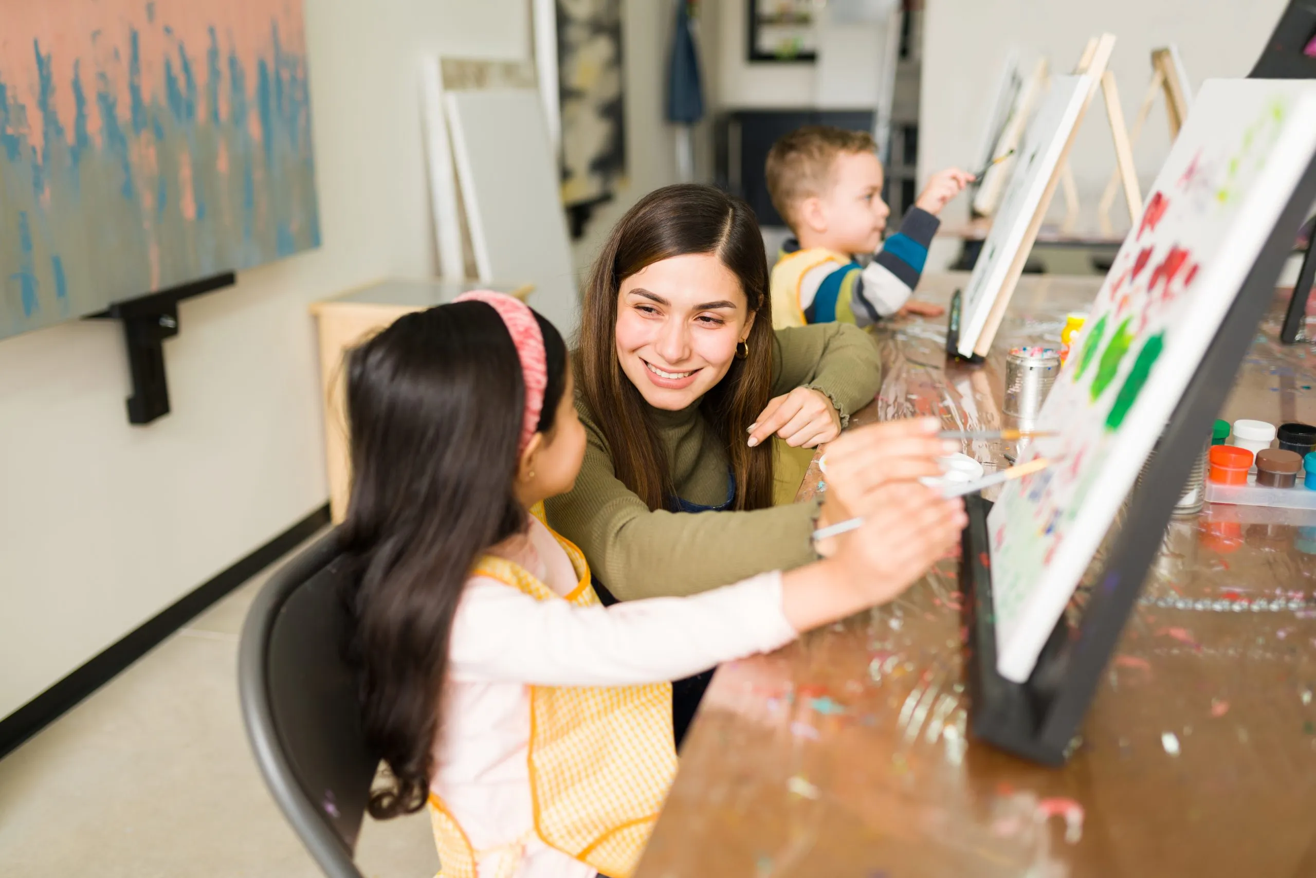 An instructor teaching a child to paint on canvas